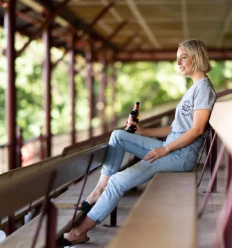 Woman drinking a Carlton Draught bottle on a bench